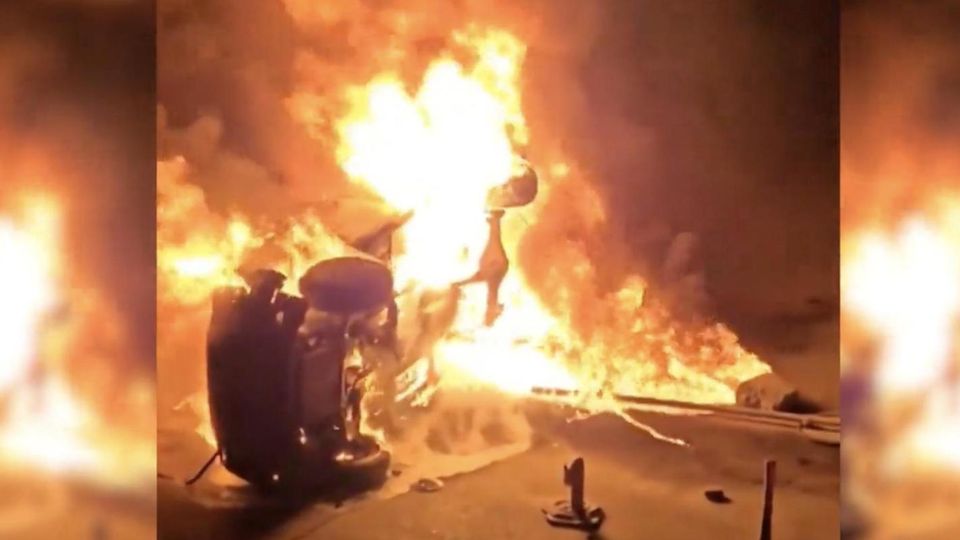 Ein brennenden Auto liegt auf der Seite.