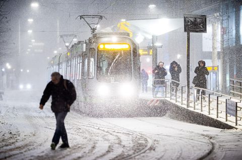Eine Straßenbahn hält am frühen Morgen im dichten Schneefall an einer Haltestelle im Zentrum von Hannover
