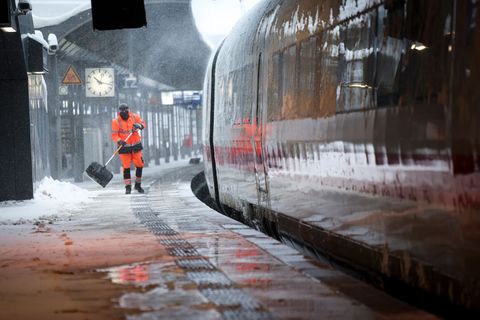 Mitarbeiter schieben Schnee von einem Bahnsteig am Hamburger Hauptbahnhof. Foto: Christian Charisius/dpa