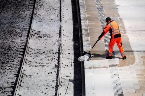 Ein Mann räumt am Hauptbahnhof in Hamburg auf einem Bahnsteig Schnee. Foto: Daniel Bockwoldt/dpa