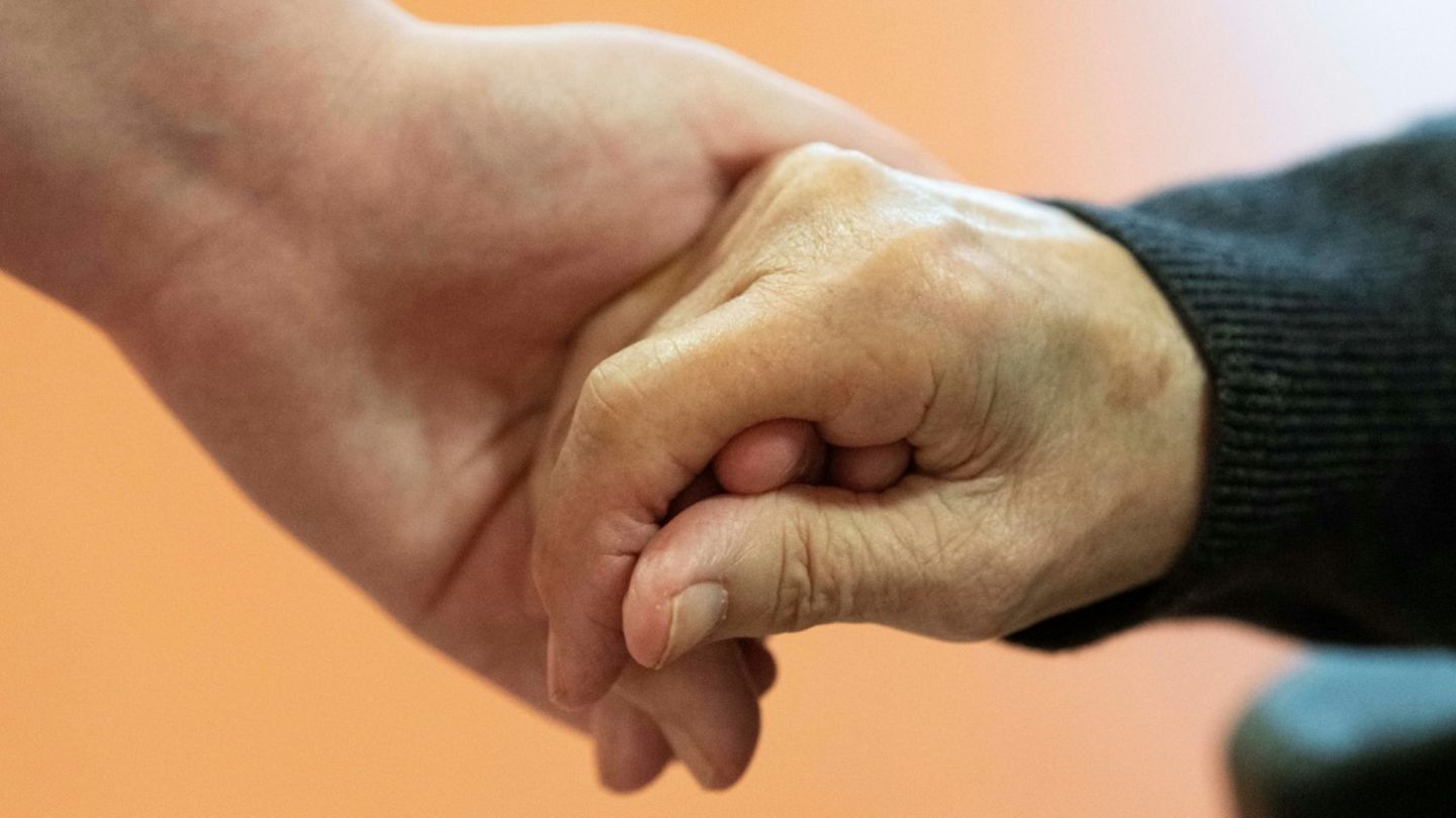 Pflegerin hält die Hand eines alten Mannes