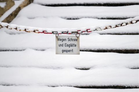 "Wegen Schnee und Eisglätte gesperrt" steht auf einem Schild über einer verschneiten Treppe – Glatteis