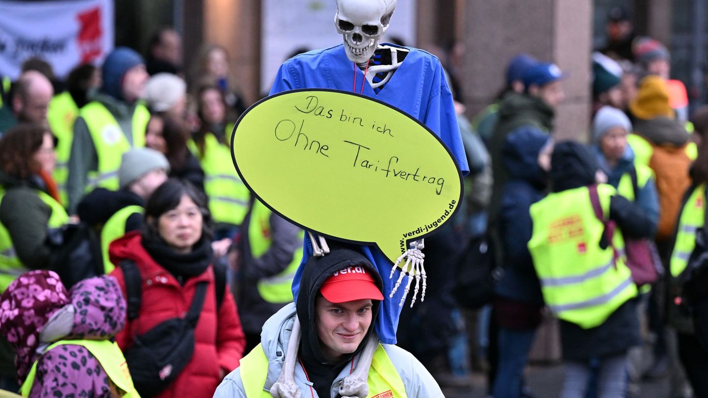Beschäftigte der Uniklinik Köln halten bei einem Warnstreik ein Skelett mit dem Schild "Das bin ich ohne Tarifvertrag" in die Hö