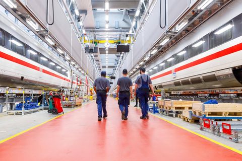 Drei Mitarbeiter in einem Werk der Deutschen Bahn laufen durch die Werkhalle