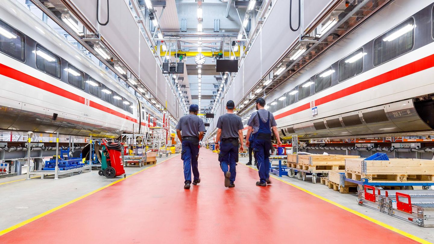 Drei Mitarbeiter in einem Werk der Deutschen Bahn laufen durch die Werkhalle