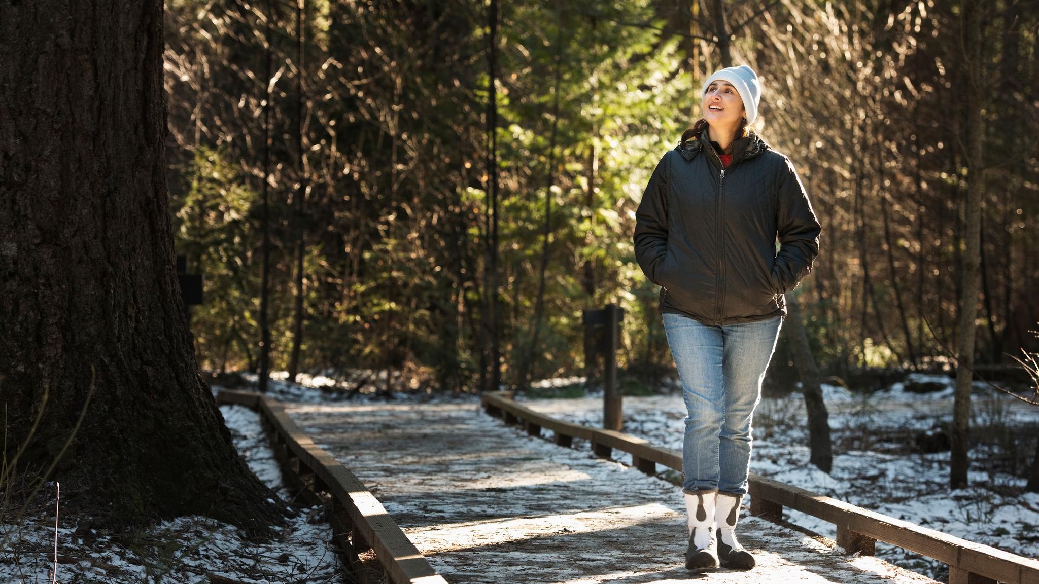 Eine Frau mit weisser Mütze wandert im Winter auch den Wald