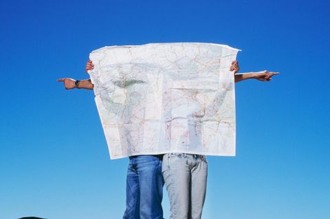 Gen Z Zwei Menschen verbergen sich hinter einer großen Landkarte, sie deuten in unterschiedliche Richtungen