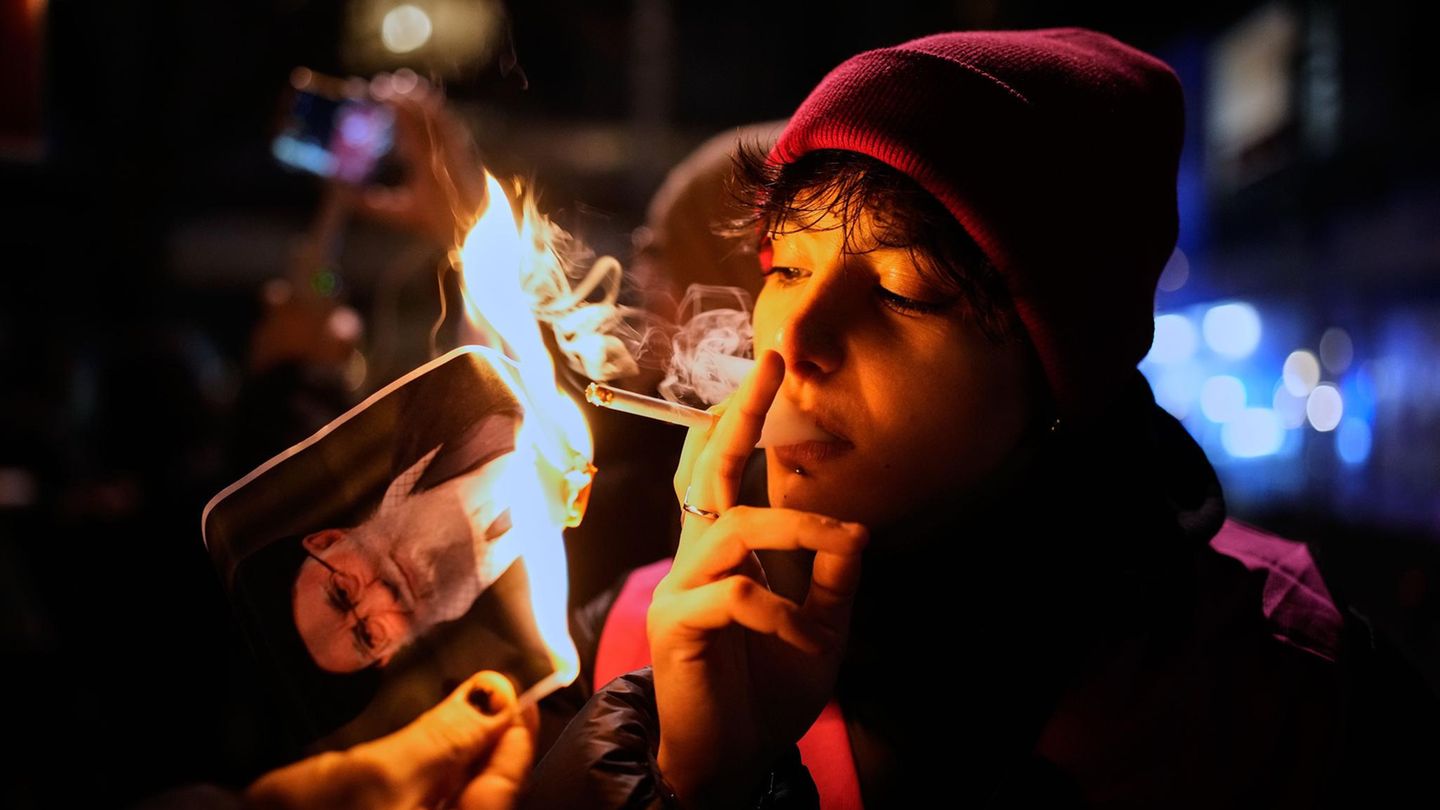 Ein Demonstrant zündet sich eine Zigarette an einem brennenden Plakat von Irans Oberstem Führer Ayatollah Ali Khamenei an