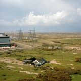 Eine Landschaft von oben, in der man grüne Wiesen sieht, ein Haus und in der Ferne Strommasten