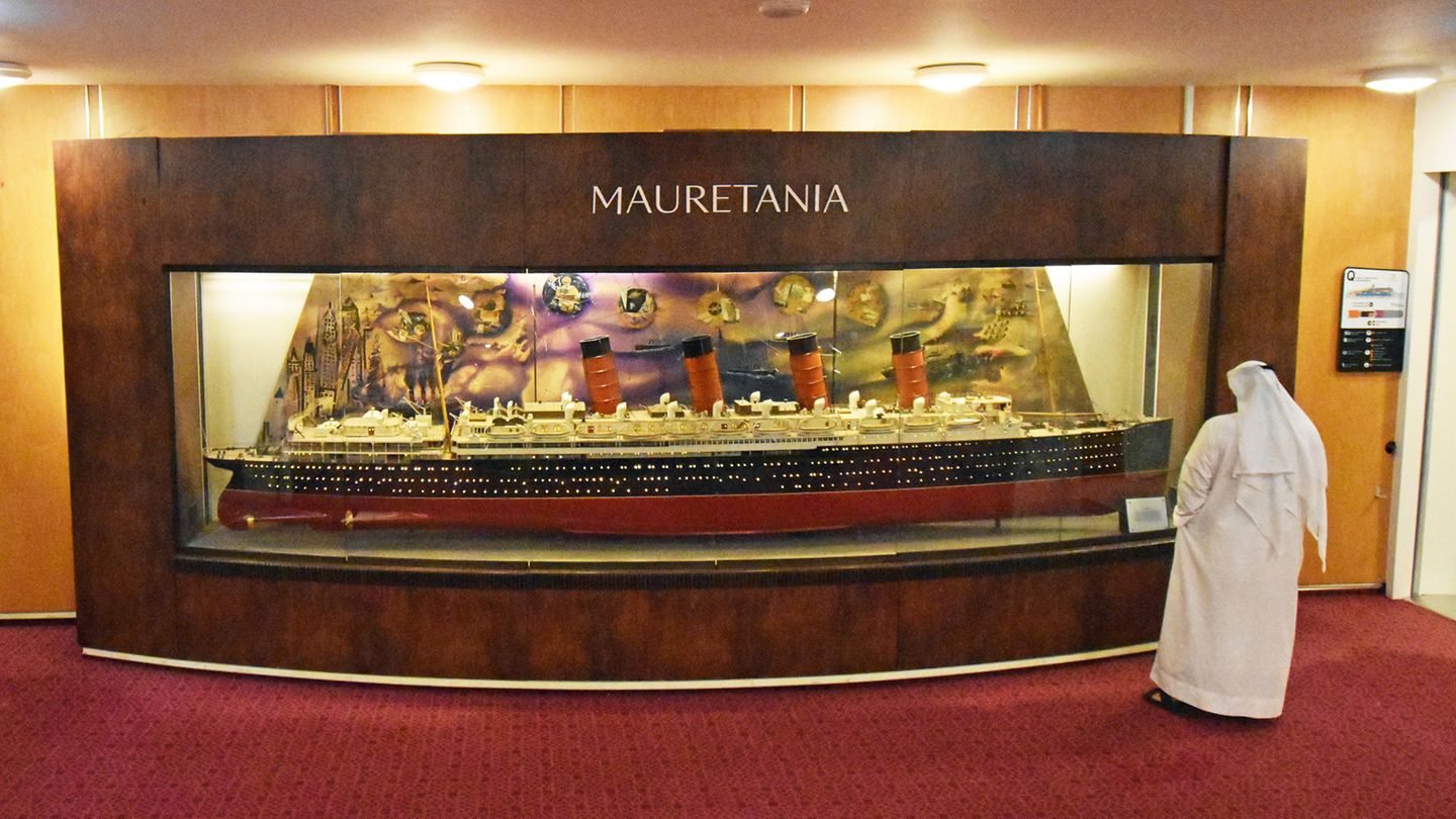 Ein Mann in traditionellem, langem weißen Gewand betrachtet das Modell-Schiff