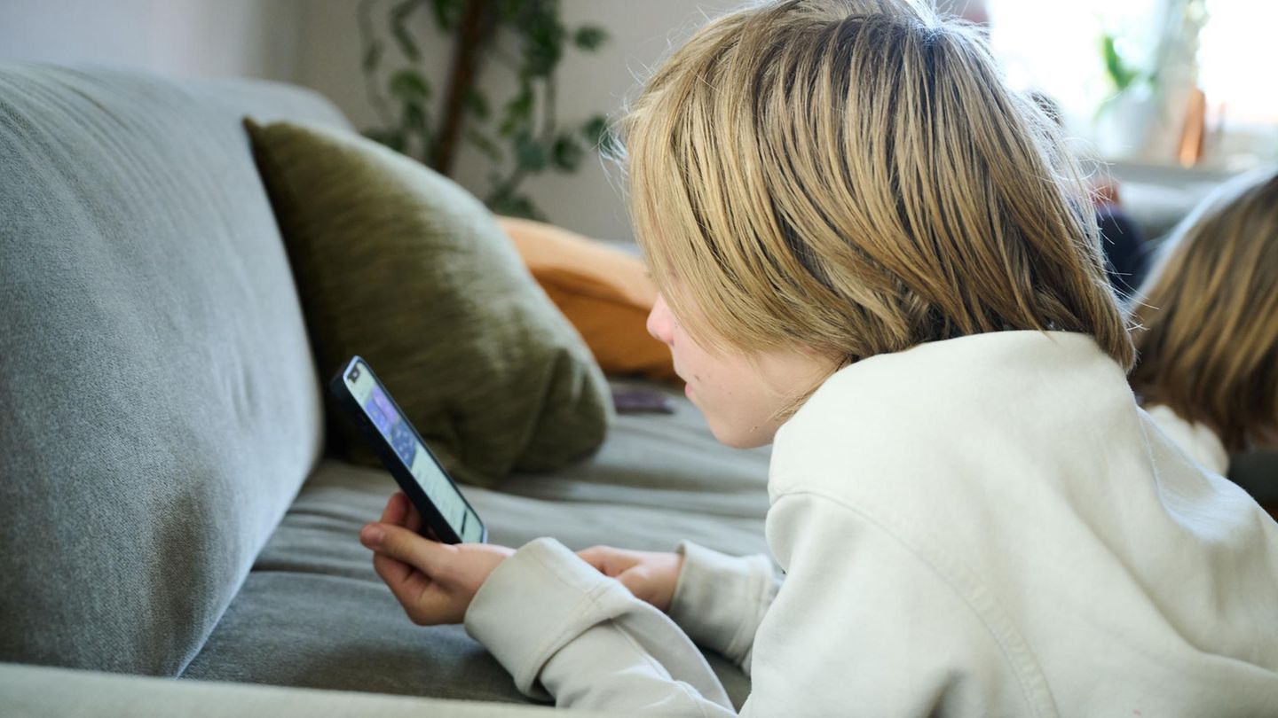 Ein Junge liegt auf dem Sofa und guckt auf ein Smartphone