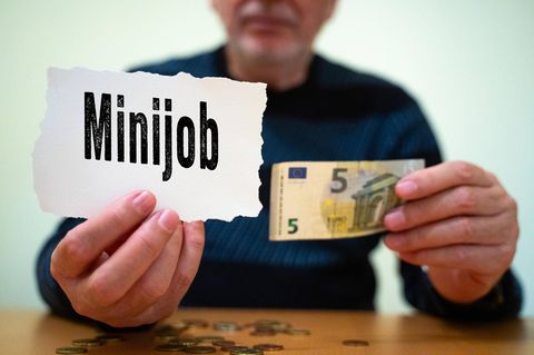 Eine Person hält ein Schild mit dem Wort "Minijob" darauf und einen 5-Euro-Schein
