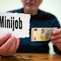 Eine Person hält ein Schild mit dem Wort "Minijob" darauf und einen 5-Euro-Schein