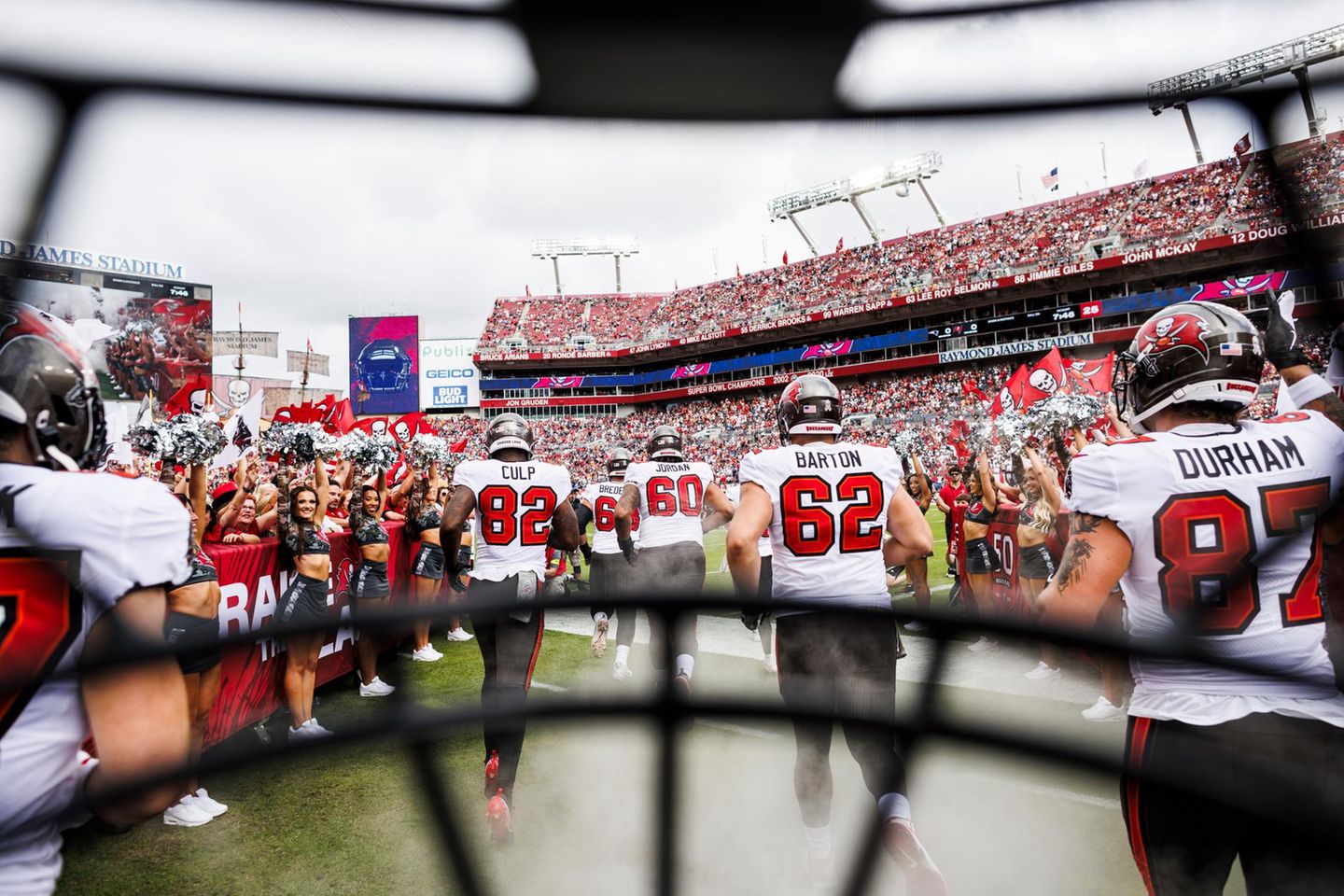 Auftakt eines American-Football-Matches: Die Tampa Bay Buccaneers laufen an den Cheerleadern vorbei auf das Feld, zur obligatorischen Vorstellung der Teams vor dem Beginn des Spiels. Das ungewöhnliche Foto dazu schoss Kyle Zedaker, indem er seine Kamera hinter dem Helmgitter befestigte – und so den Betrachtenden einen beinahe intimen, authentischen Einblick verschaffte, weil er die Perspektive der Profis einnahm   