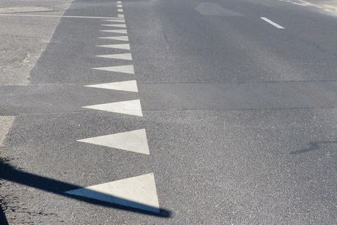 Verkehrszeichen: Eine Reihe aus weißen Dreiecken sind auf den Asphalt einer Straße gemalt.