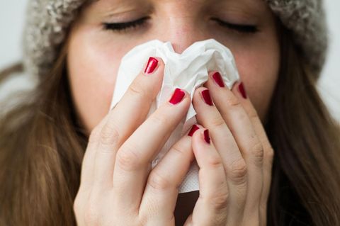 Eine junge Frau hält sich ein Papiertaschentuch vor das Gesicht