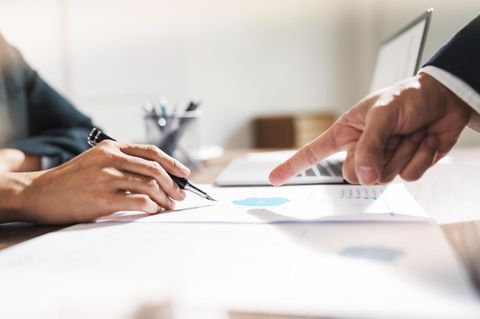 Nahaufnahme zweier Hände; eine zeigt auf ein Papier mit Gewinnzahlen