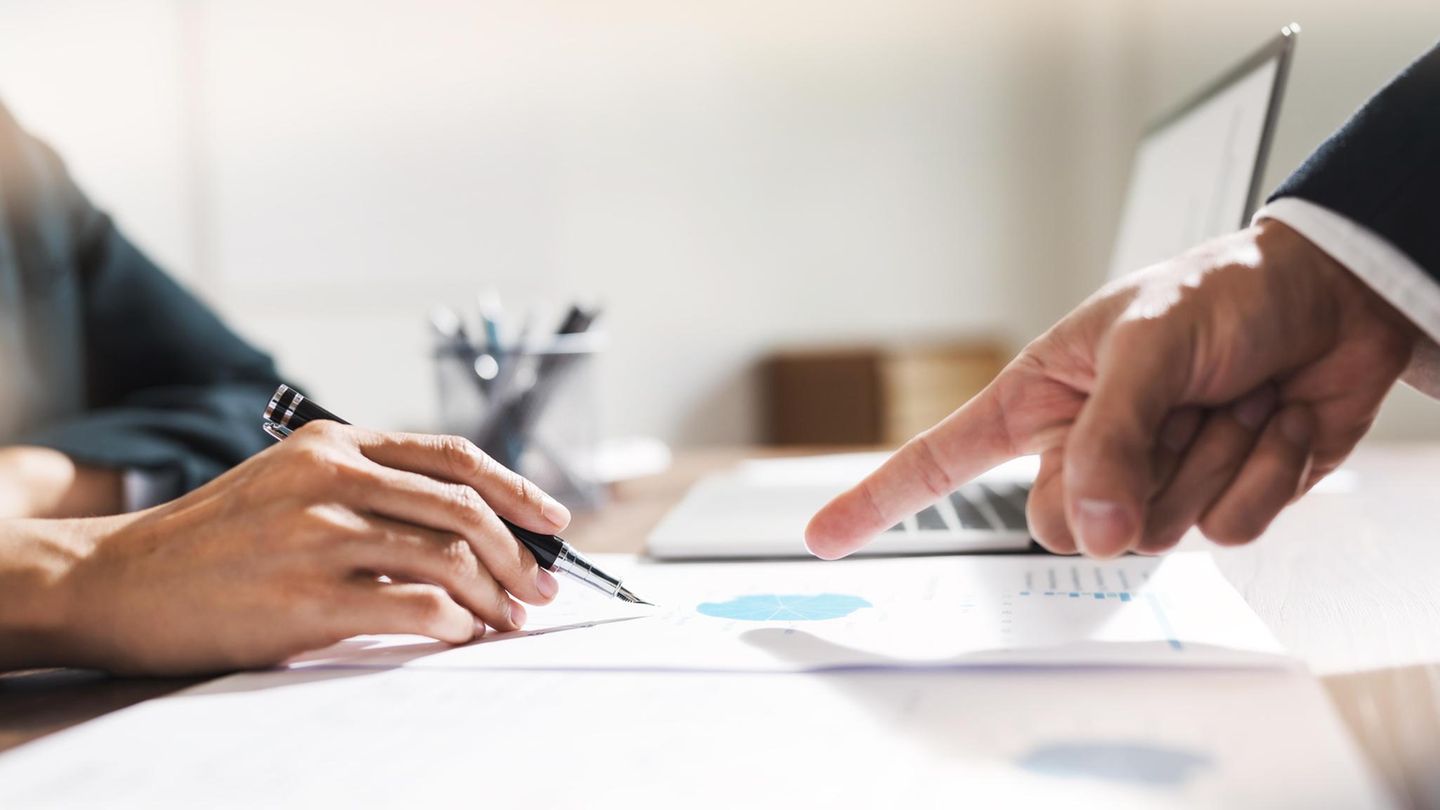 Nahaufnahme zweier Hände; eine zeigt auf ein Papier mit Gewinnzahlen