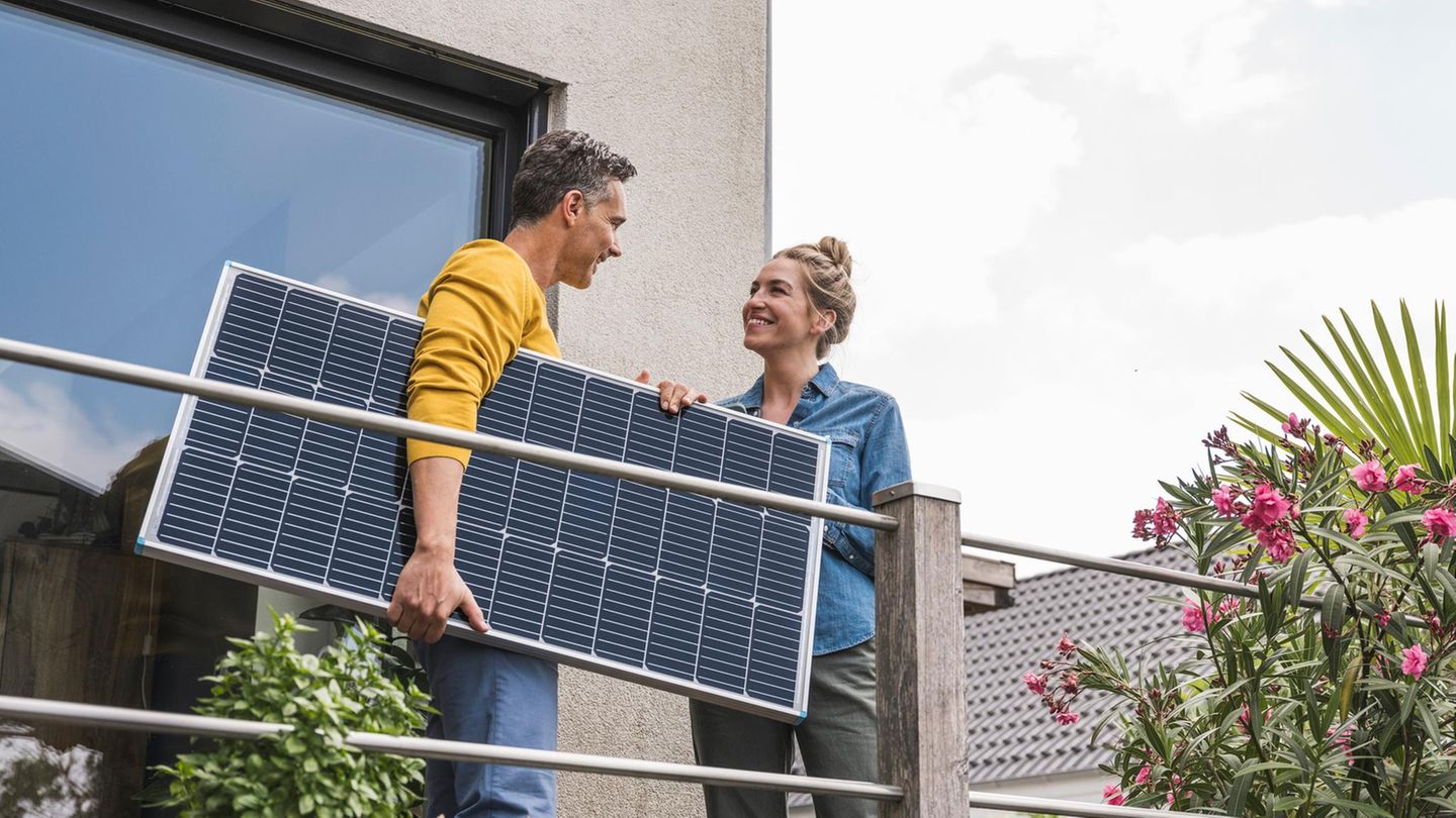 Zwei Personen stehen auf einem Balkon, der Mann hält ein Solarpanel in der Hand, die junge Frau lacht.