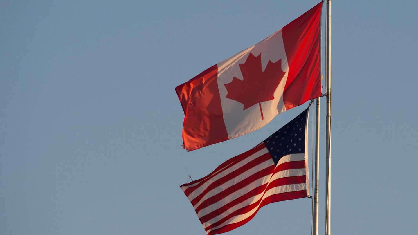 Die Flaggen von Kanada und den USA wehen nebeneinander unter blassblauem Himmel