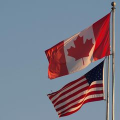 Die Flaggen von Kanada und den USA wehen nebeneinander unter blassblauem Himmel