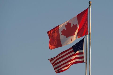 Die Flaggen von Kanada und den USA wehen nebeneinander unter blassblauem Himmel