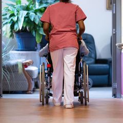 Pflegerin schiebt eine Person im Rollstuhl über den Flur eines Pflegeheims