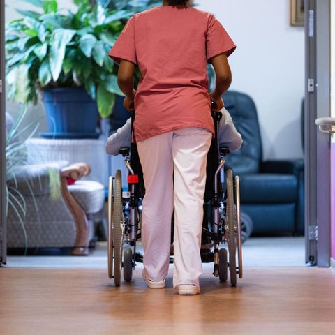 Pflegerin schiebt eine Person im Rollstuhl über den Flur eines Pflegeheims