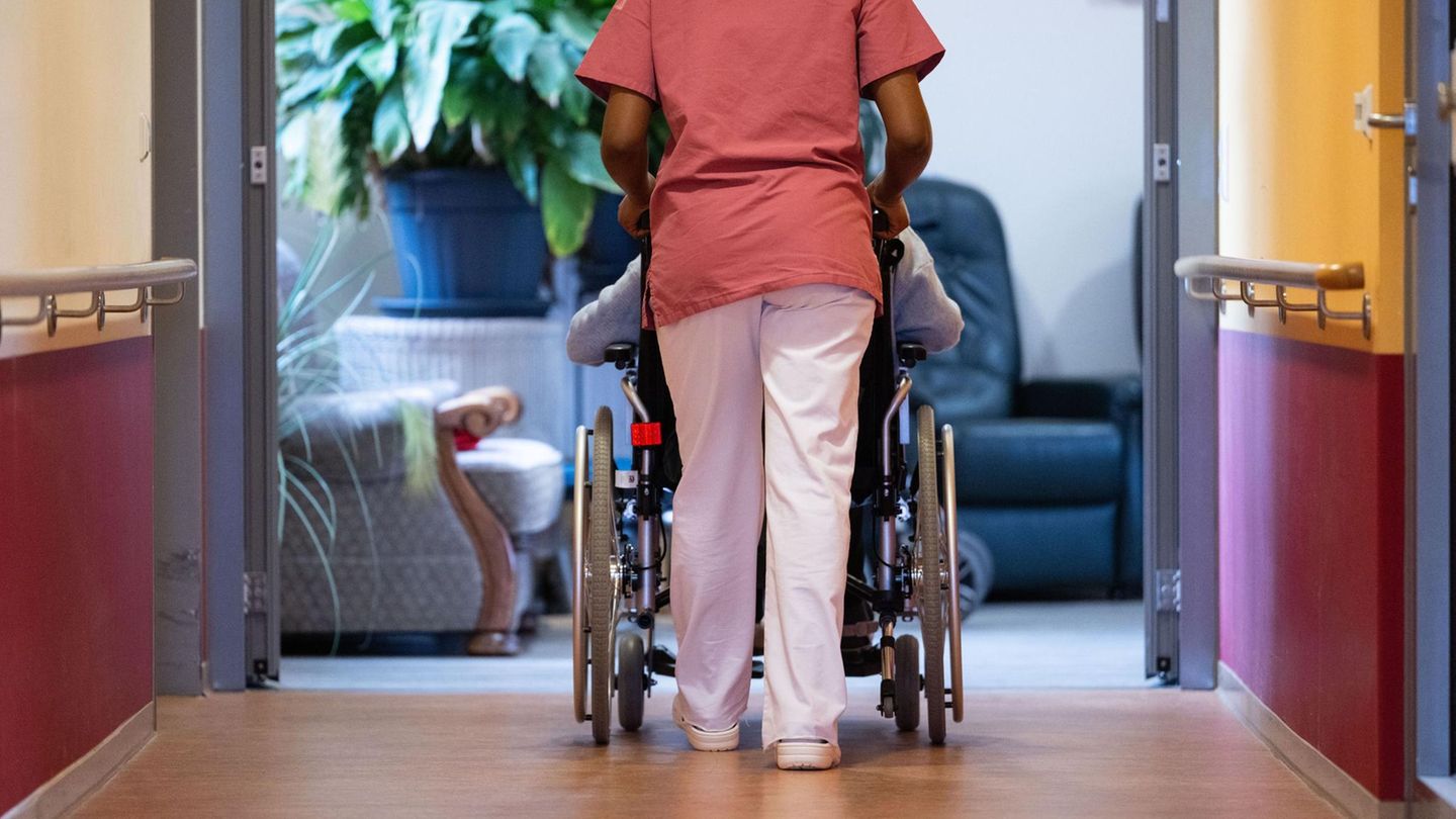 Pflegerin schiebt eine Person im Rollstuhl über den Flur eines Pflegeheims