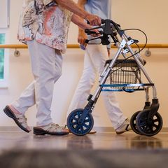 Eine Pflegekraft geht in einem Pflegeheim mit einer älteren Frau über einen Korridor