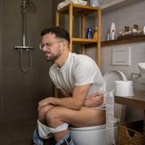 Ein Mann sitzt auf Toilette und presst