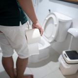 Ein Mann steht mit einer Rolle Klopapier in der Hand vor einer Toilette