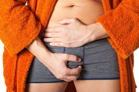 Ein Mann in Unterhose umfasst mit einer Hand sein Gemächt