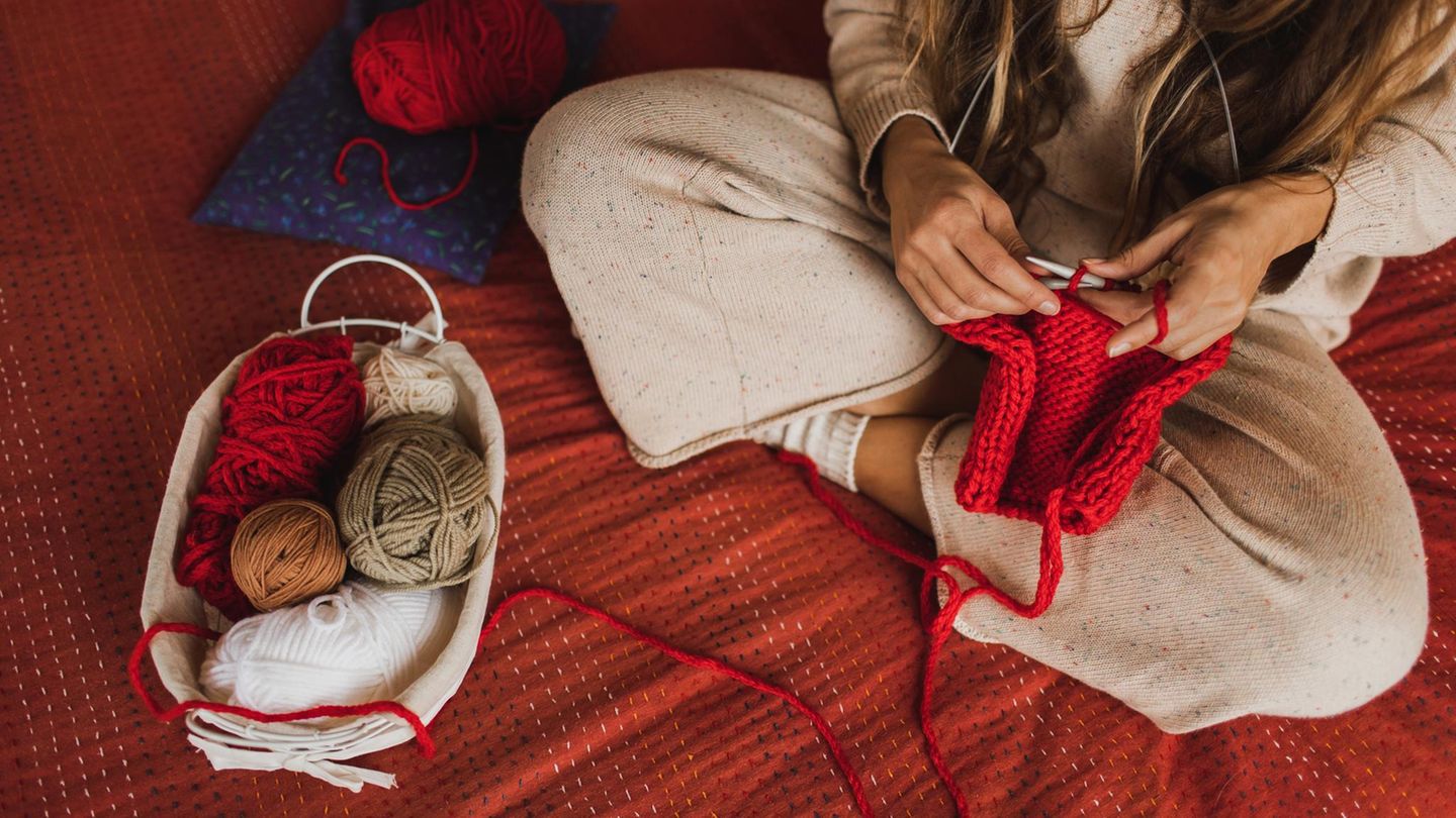 Eine Person sitzt im Schneidersitz und strickt mit roter Wolle