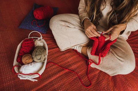 Eine Person sitzt im Schneidersitz und strickt mit roter Wolle