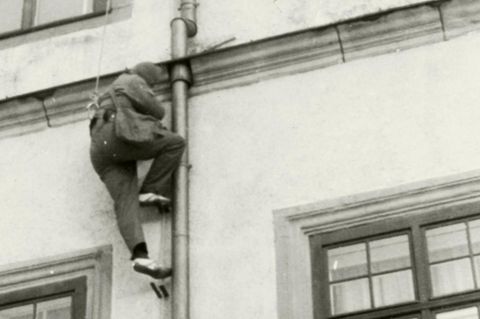 Ein Mann klettert an einer Regenrinne eine Hauswand hoch