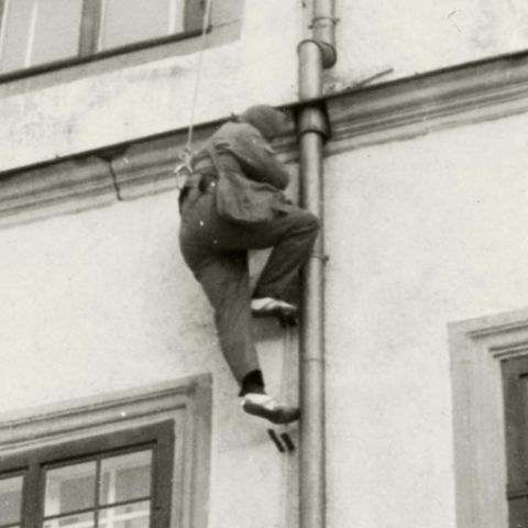 Ein Mann klettert an einer Regenrinne eine Hauswand hoch