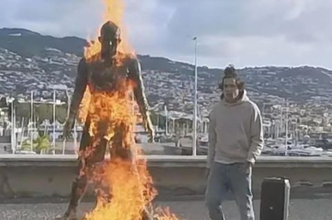 Ein Mann tanzt neben einer brennenden Ronaldo Statue.