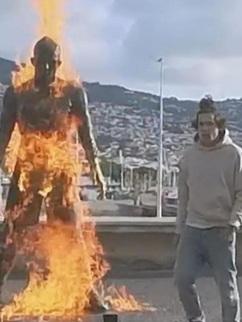 Ein Mann tanzt neben einer brennenden Ronaldo Statue.