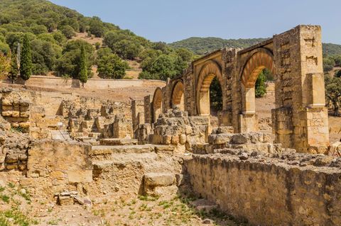 Ruinen der Palaststadt Madinat al-Zahrā aus hellem Gestein. Auf der rechten Seite vier Torbögen mit roten Verzierungen.