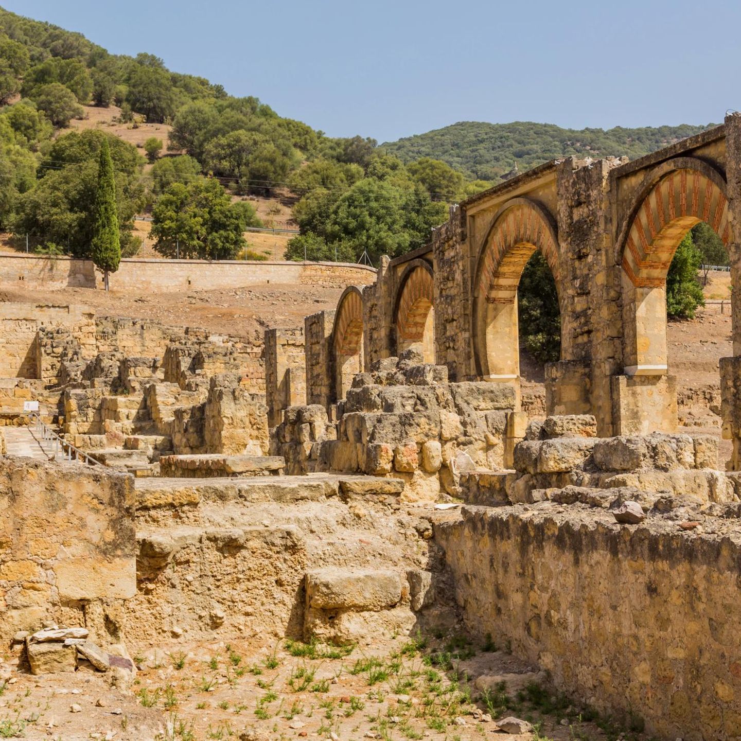 Ruinen der Palaststadt Madinat al-Zahrā aus hellem Gestein. Auf der rechten Seite vier Torbögen mit roten Verzierungen.
