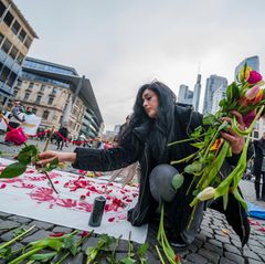 Eine Frau legt auf einer Kundgebung gegen das Regime im Iran auf dem Rathenauplatz Rosen nieder