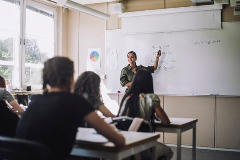 Junge Referendarin steht vor den Schülern und erklärt an der Tafel