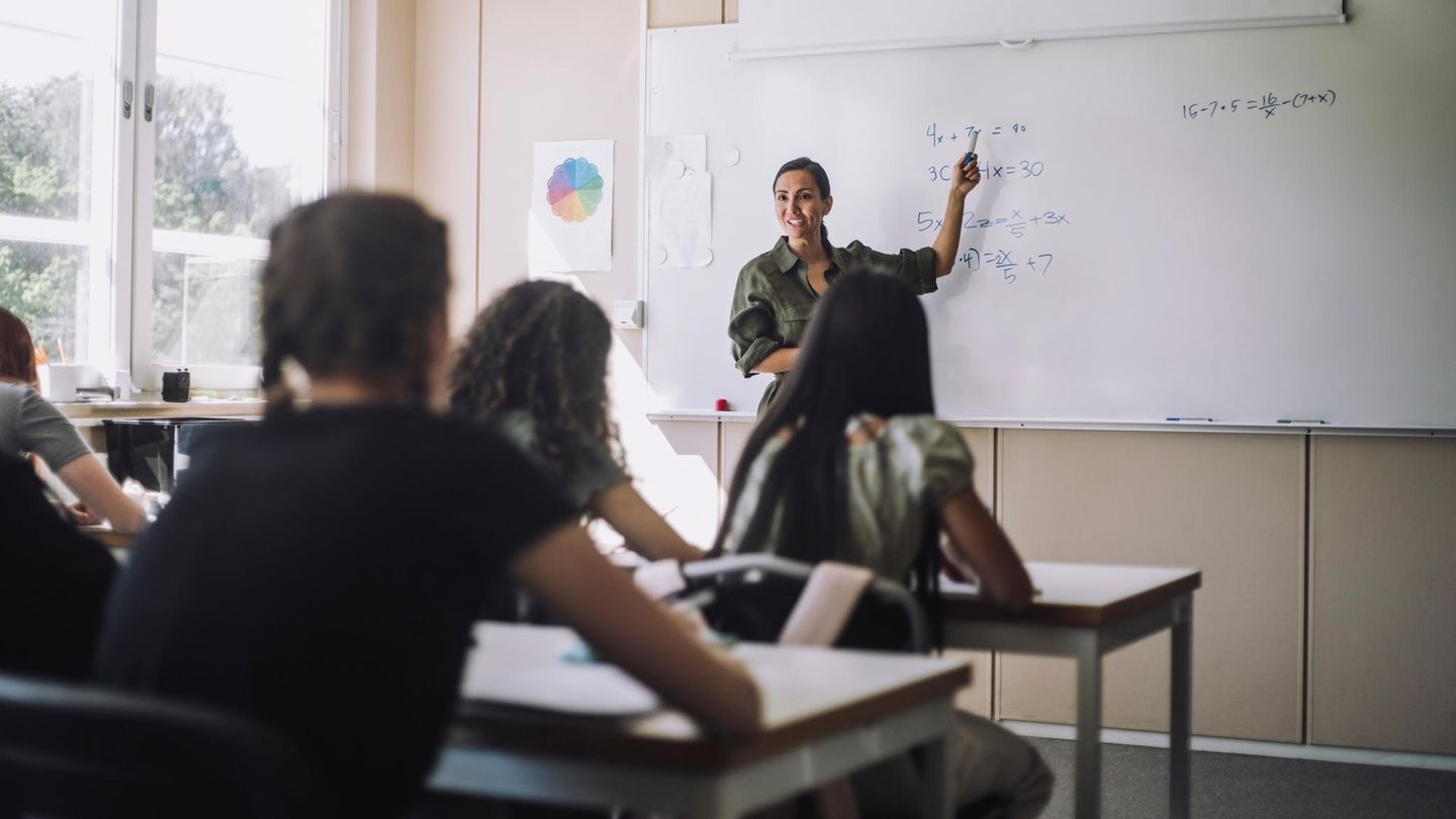 Junge Referendarin steht vor den Schülern und erklärt an der Tafel