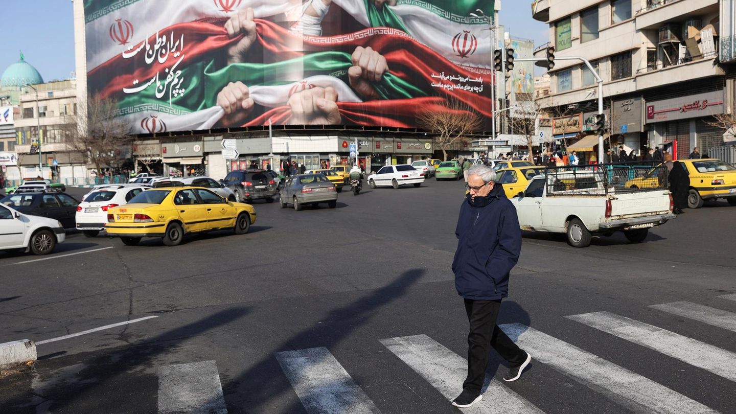 Ein Mann läuft über eine Straßenkreuzung in Teheran, im Hintergrund ein Propaganda Plakat
