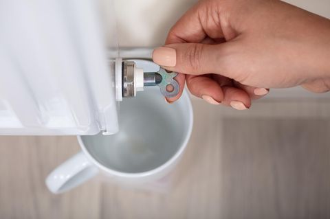 Nahaufnahme der Hand einer Person, die das Heizkörperentlüftungsventil dreht, um Luft mit Becher abzulassen