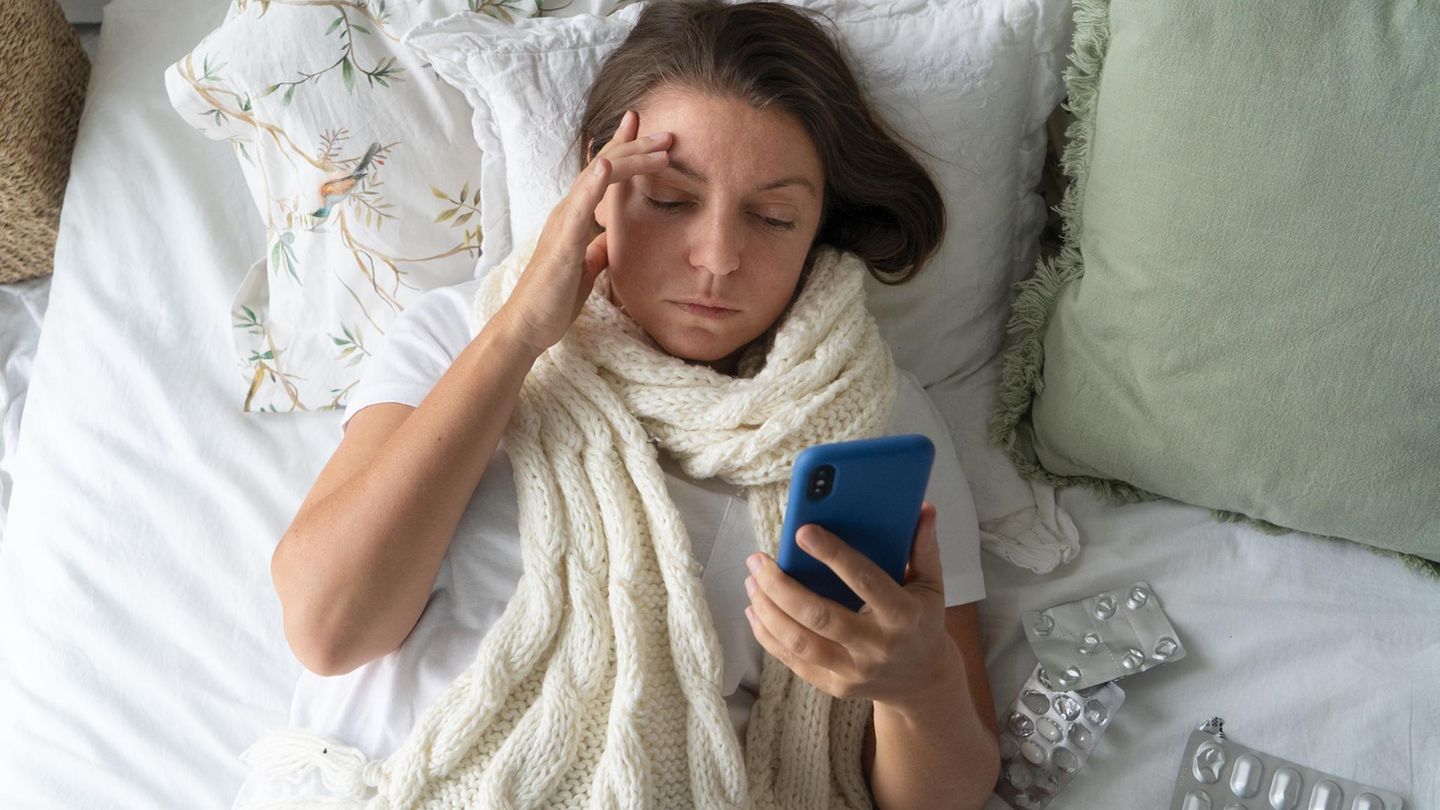 Eine Frau liegt krank im Bett und will telefonieren (Symbolbild Krankmeldung)