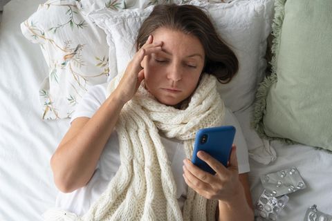 Eine Frau liegt krank im Bett und will telefonieren (Symbolbild Krankmeldung)