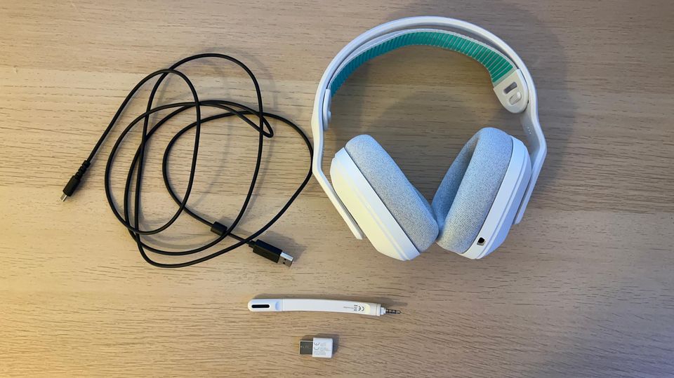 Weiße Kopfhörer und ein schwarzes Kabel liegen neben dem Wireless-Dongle und dem Mikro bei