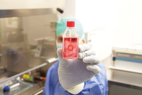 Gewebespende: Eine Person mit Mundschutz und Laborkleidung hält eine Flasche mit rötlicher Flüssigkeit hoch
